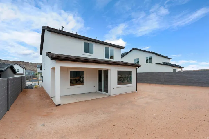 Two-story stucco exterior featuring a covered patio, dark roof, and perimeter fencing