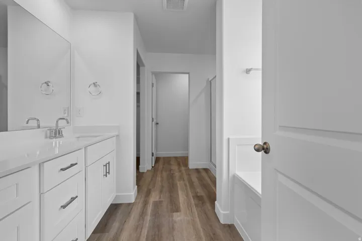 White shaker cabinetry with brushed nickel hardware, light-toned countertop, wood-finish flooring, and a built-in tub
