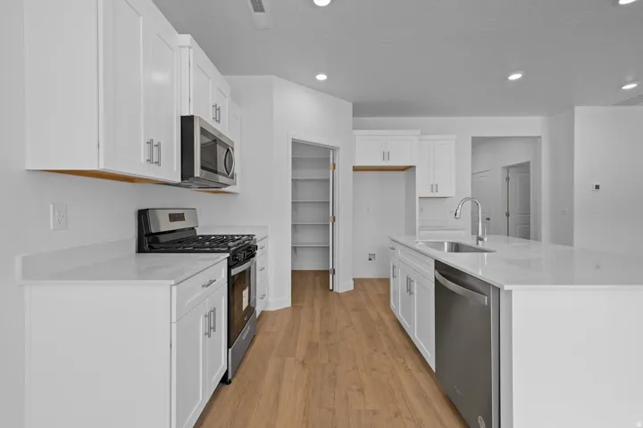 Modern kitchen featuring white cabinetry, stainless steel appliances, light-toned countertops, wood-finish flooring, and recessed lighting