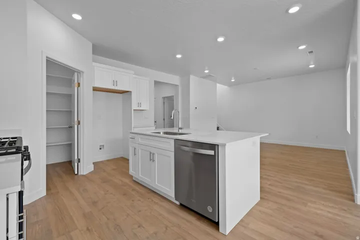Kitchen island with counter seating, stainless steel dishwasher, white shaker cabinetry, wood-finish flooring, and recessed lighting