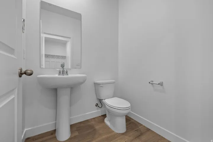 Pedestal sink with chrome faucet, wall-mounted mirror, white toilet, and wood-finish flooring