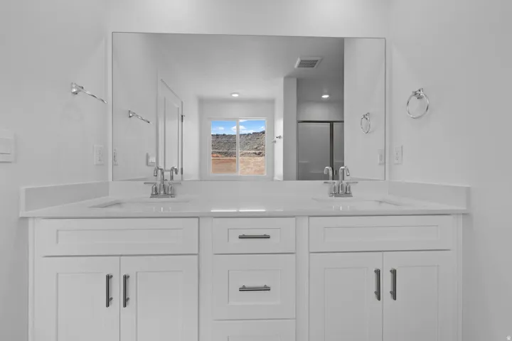 Dual vanity with white cabinetry, integrated sinks, chrome fixtures, and a large wall-mounted mirror