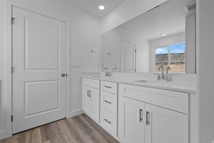 Dual vanity with white cabinetry, wood-finish flooring, and a large wall-mounted mirror