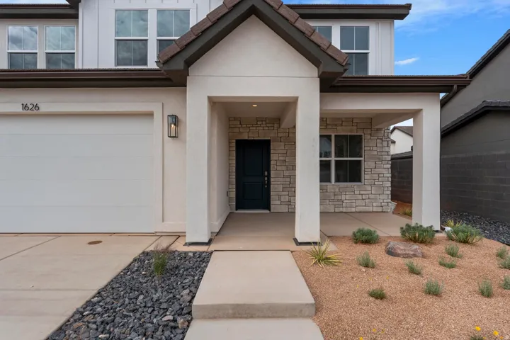 Modern exterior featuring a prominent covered entry, stone veneer accents, and a panel garage door with an adjacent wall sconce