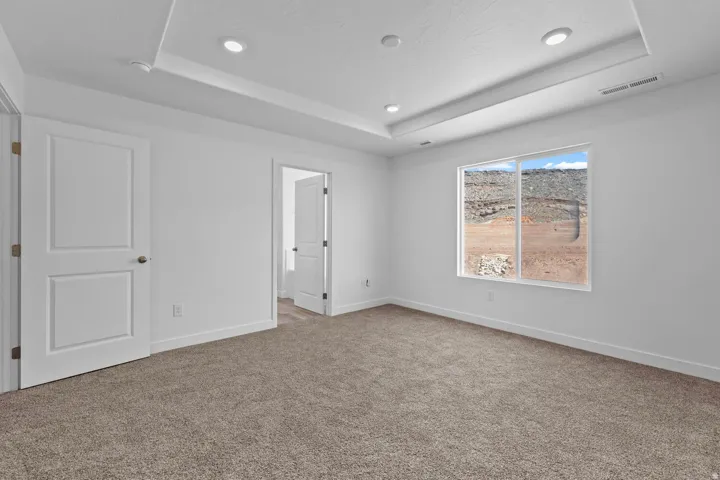 Recessed lighting, tray ceiling, neutral carpet, white paneled doors, and a large window