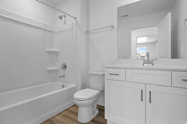 Bathroom featuring a white vanity with a light-colored countertop, chrome fixtures, a shower-tub combination with a white surround, and wood-finish flooring