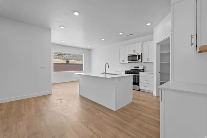 Kitchen featuring white cabinetry, stainless steel appliances, a center island with sink, and wood-finish flooring