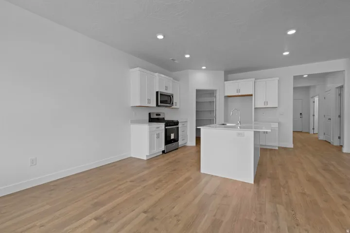 Open-concept living space with wood-finish flooring, recessed lighting, white cabinetry, a kitchen island, and stainless steel appliances
