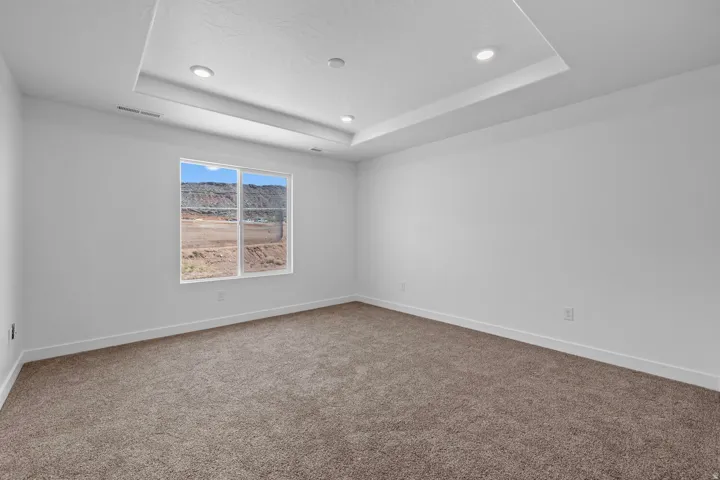 Tray ceiling with recessed lighting, wall-to-wall carpeting, and a window with a mountain backdrop