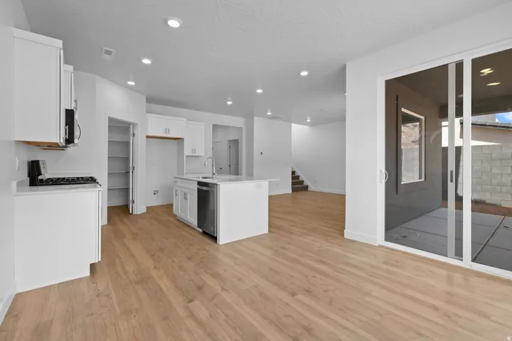 Kitchen featuring white cabinetry, stainless steel appliances, a central island with sink, wood-finish flooring, and sliding glass door access to a patio