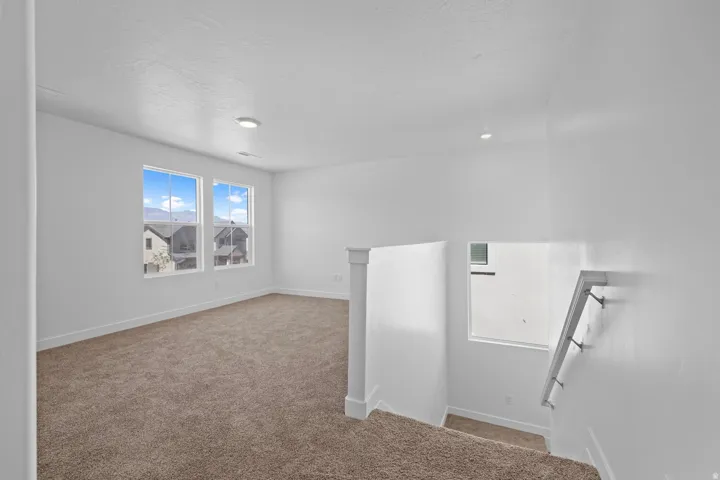Carpeted open area with recessed lighting, two windows, and a staircase featuring a modern handrail