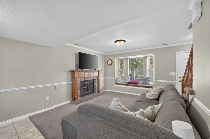 Built-in bay window bench, wood-mantled fireplace, brick hearth, carpeted flooring, and a ceiling-mounted light fixture