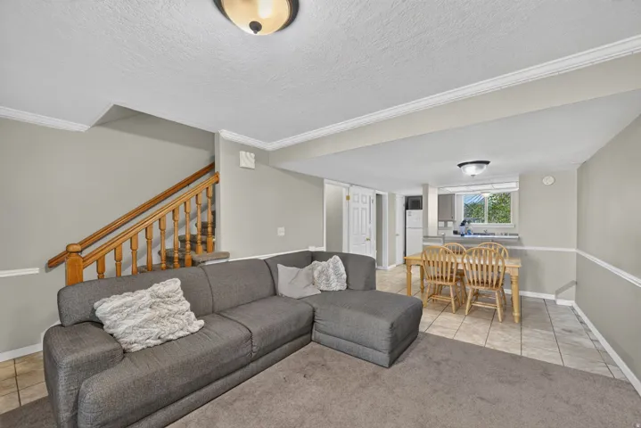 Open-concept living area featuring a wood staircase, crown molding, and tiled flooring