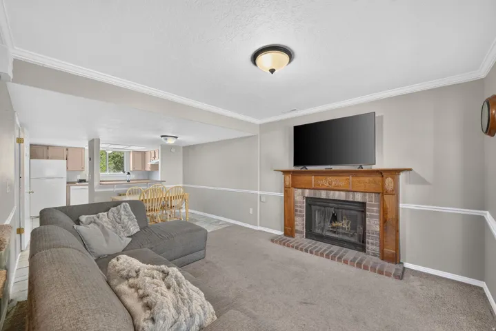 Brick fireplace with a wood-finish mantelpiece, carpeted flooring, and crown molding