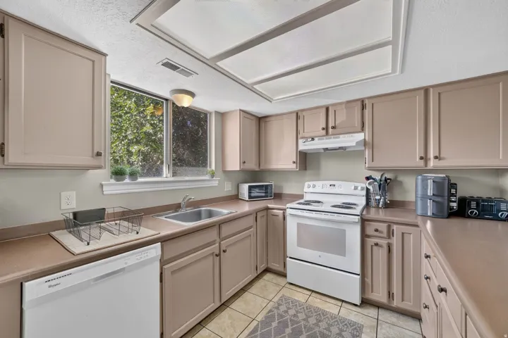 Kitchen featuring white appliances, warm-toned cabinetry, a double basin sink, and ample counter space