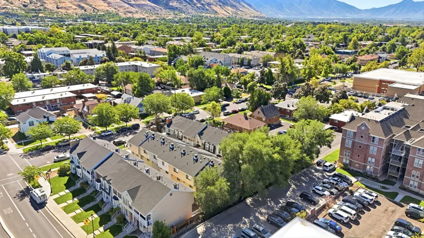 Mountain backdrop, lush green trees, townhome-style residences, multi-story building with brick facade, extensive paved parking area