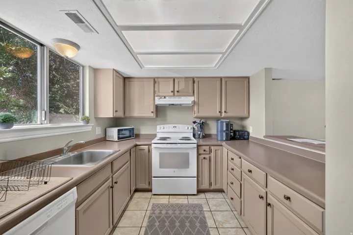 Kitchen featuring extensive cabinetry, tile flooring, a window above the sink, a built-in oven, and a range hood