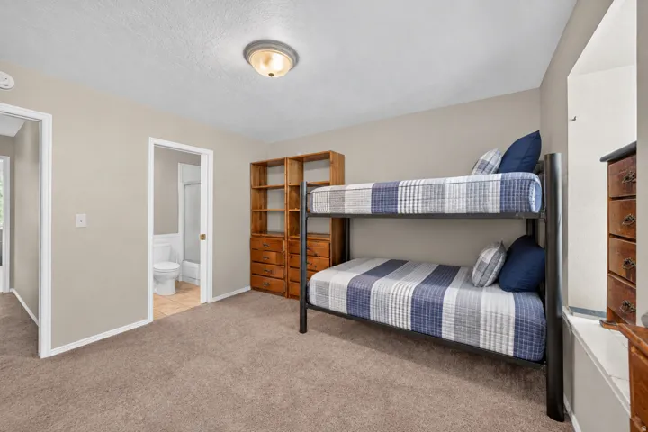 Carpeted bedroom featuring neutral wall tones, a built-in wood-finish shelving unit with drawers, and an attached bathroom with tile flooring and a shower