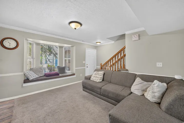 Bay window with built-in seating, neutral wall paint, carpeted flooring, and a wood-finish staircase