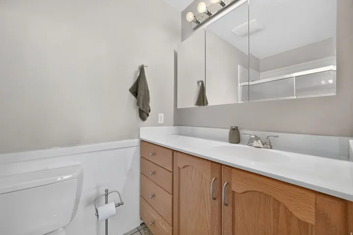 Wood-finish vanity with a built-in sink, white countertop, and a mirrored medicine cabinet
