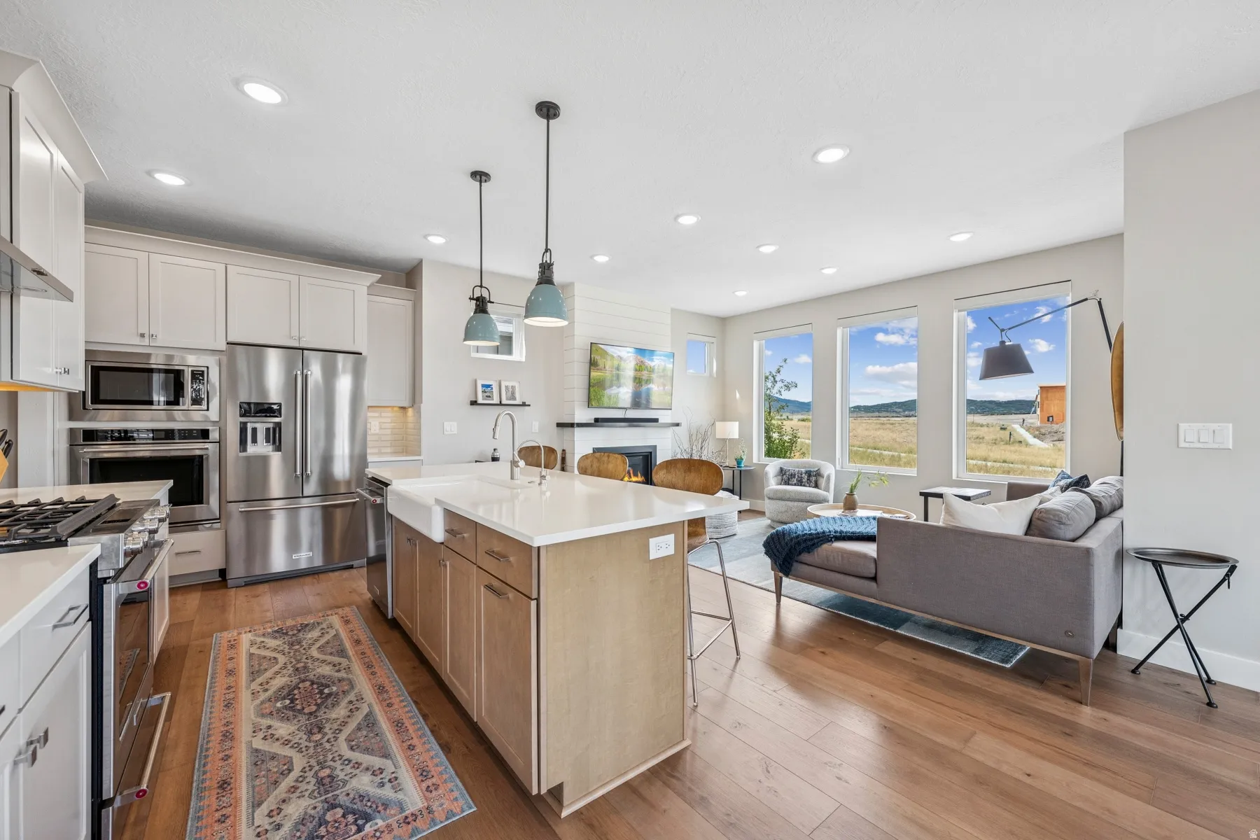 Open concept design featuring wood-finish flooring, a kitchen island with a farmhouse sink, stainless steel appliances, and abundant natural light from multiple windows