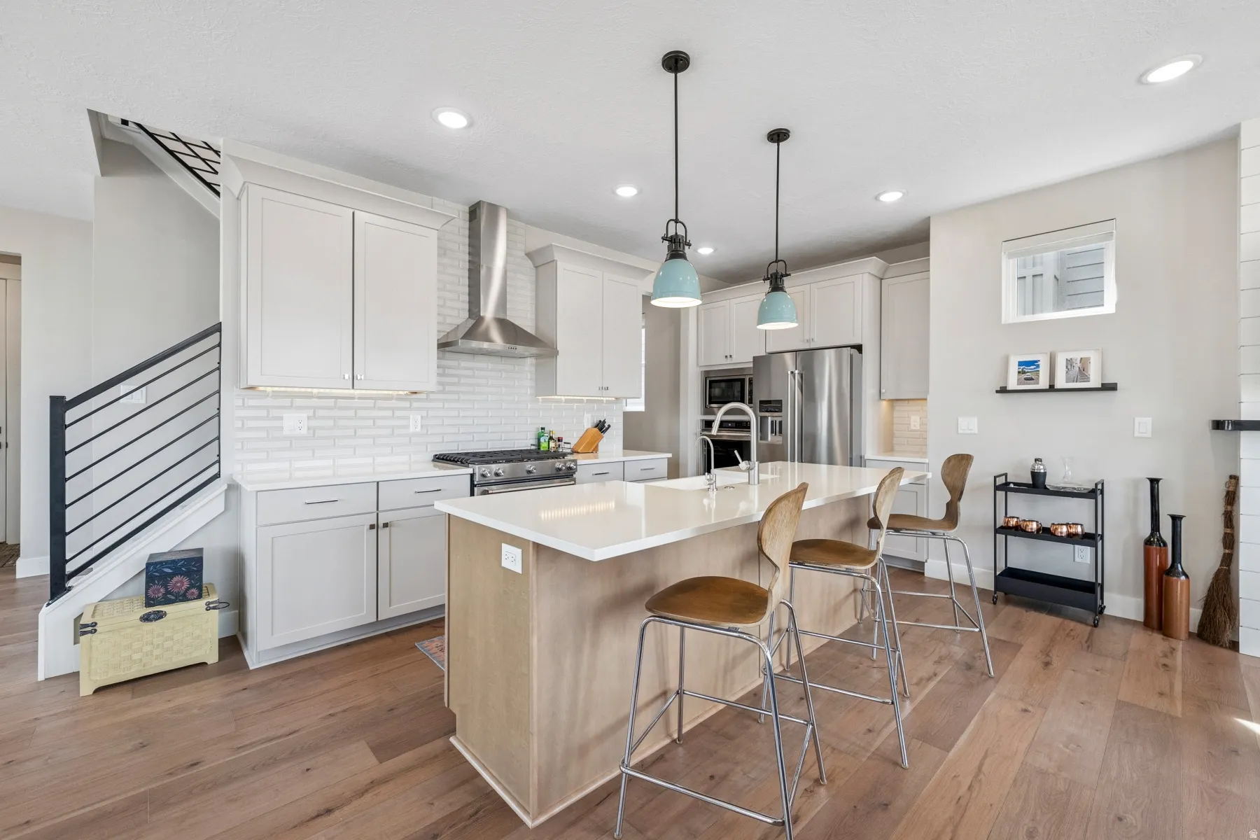 Modern kitchen featuring a central island with countertop seating, stainless steel appliances, light wood-finish flooring, white shaker cabinets, and a white subway tile backsplash