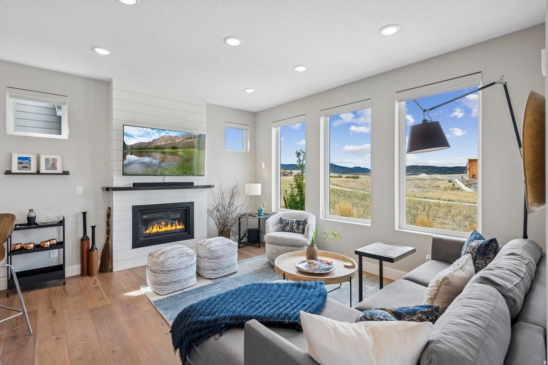Open-concept living space with wood-finish flooring, a contemporary fireplace with shiplap detailing, recessed lighting, and multiple windows offering expansive outdoor scenery