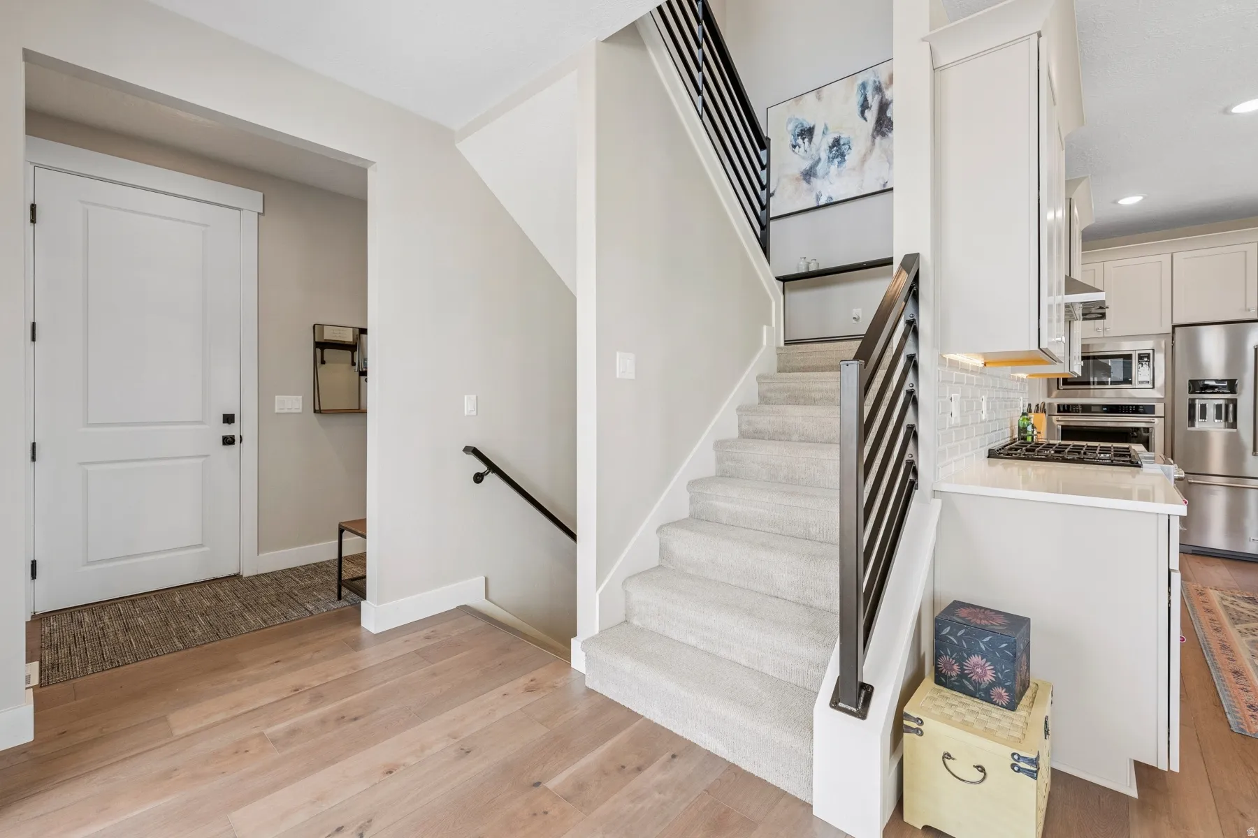 Wood-finish flooring, white paneled door, carpeted staircase, and modern black stair railings