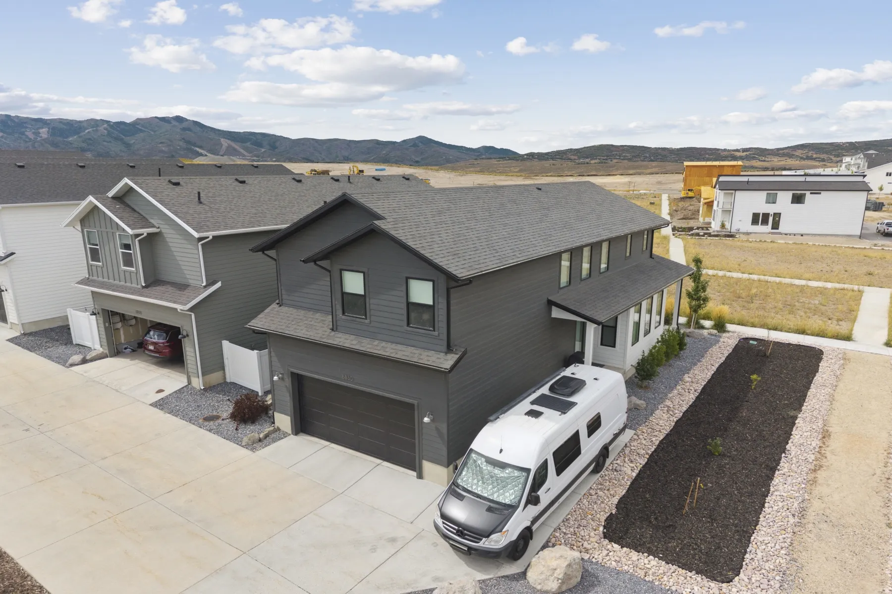 Modern two-story residence featuring a dark gray exterior, attached garage, and covered front porch