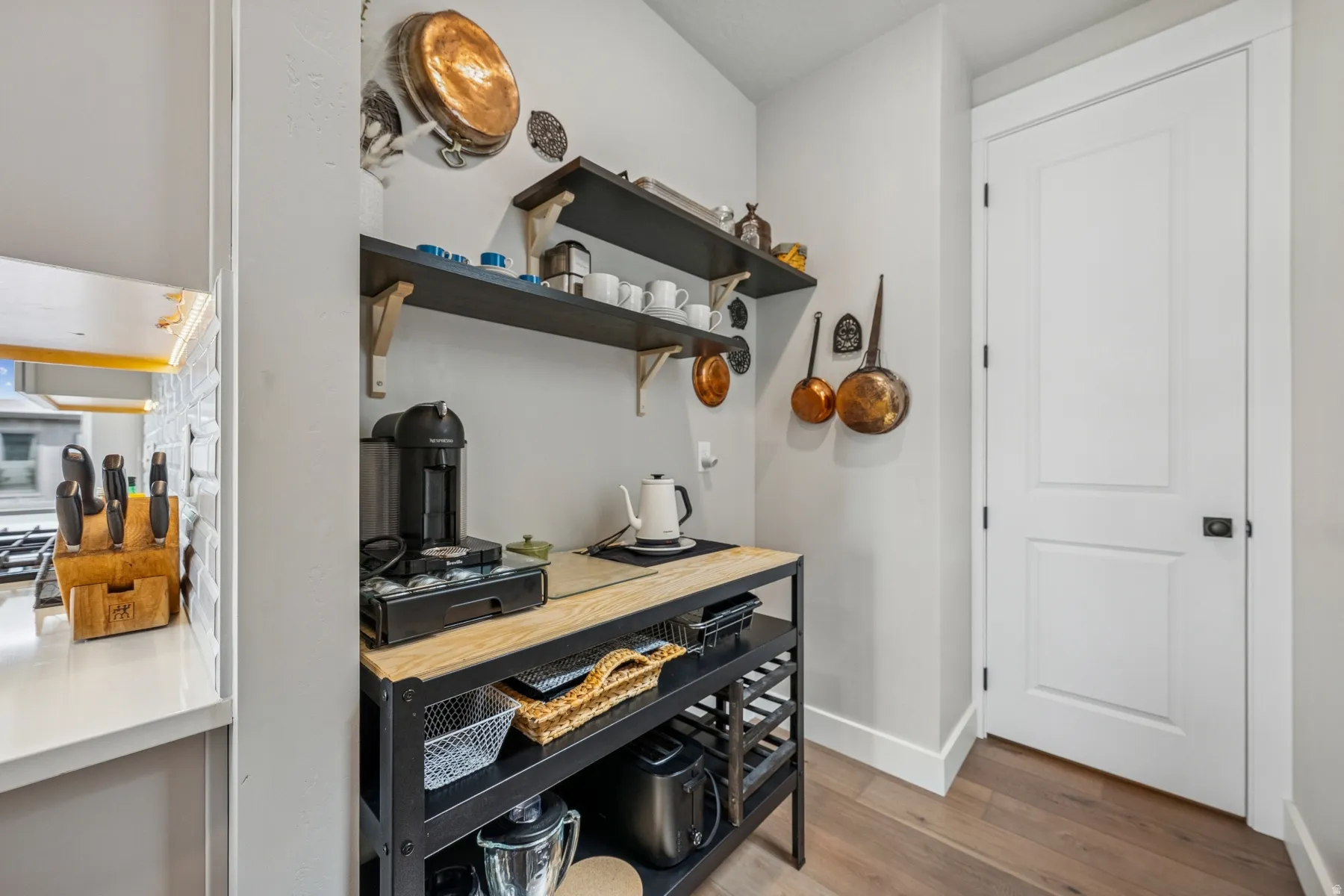 Wood-finish flooring, white paneled door with dark hardware, built-in open shelving, and a multi-level storage cart with a wood countertop