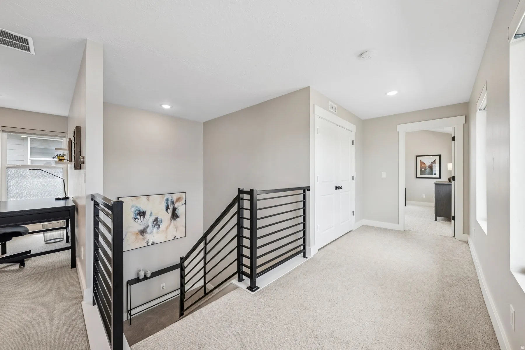 Carpeted landing with modern black horizontal bar railing, recessed lighting, and white trim