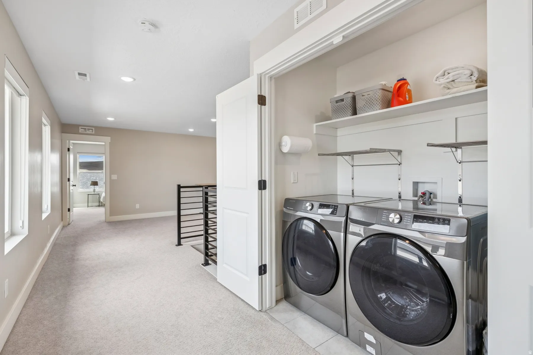 Dedicated laundry closet with built-in shelving, two large windows, recessed lighting, and a metal railing