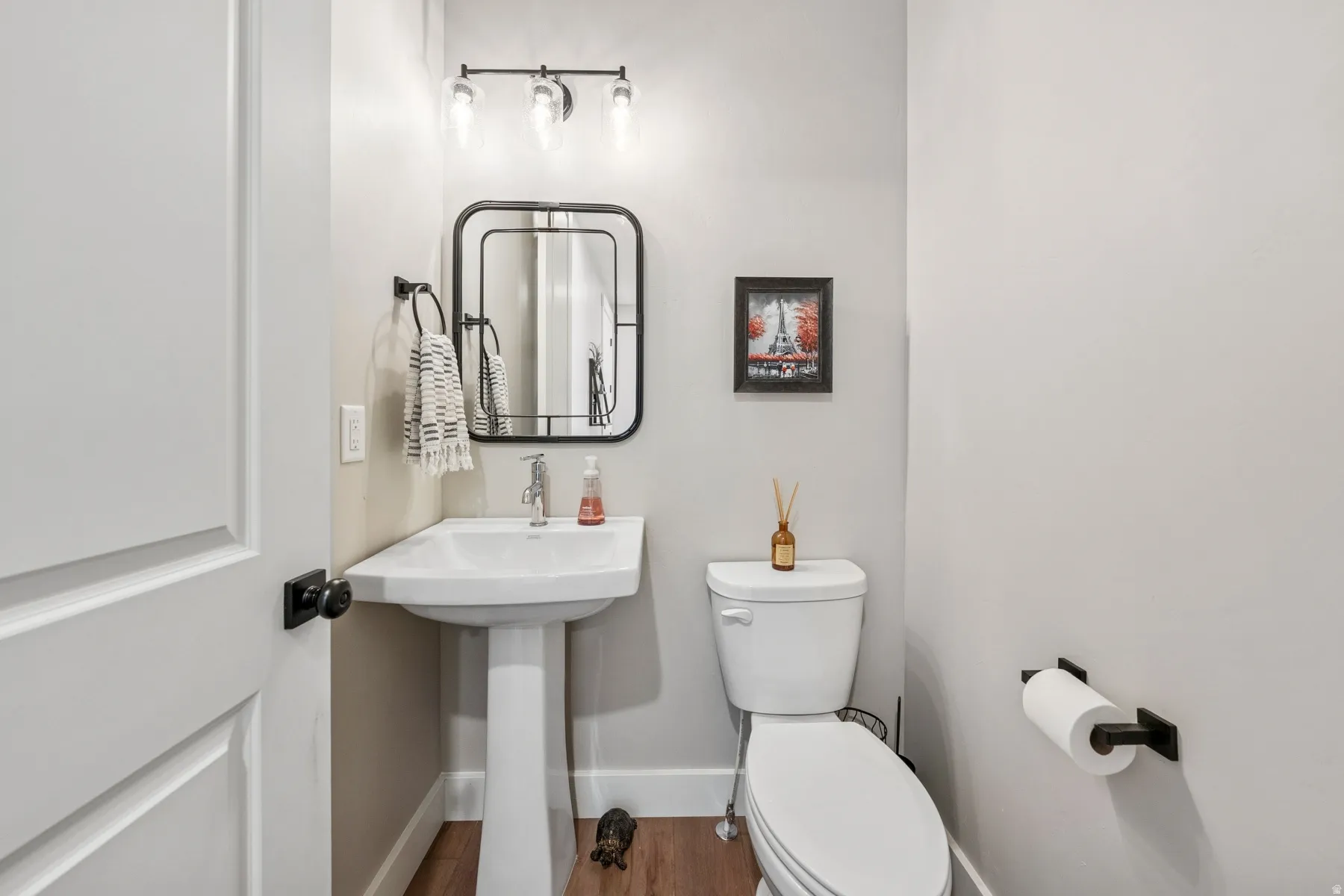 Pedestal sink with a polished chrome faucet, rectangular-framed mirror, and a three-light vanity fixture