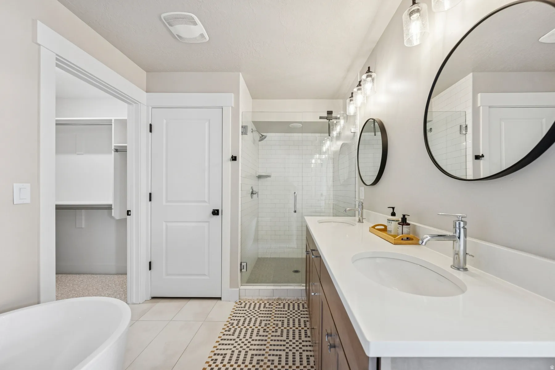 Dual vanity with undermount sinks, frameless glass shower enclosure, freestanding soaking tub, and custom-built closet shelving