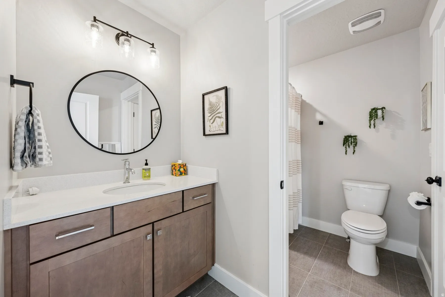 Vanity with integrated sink and stone-finish countertop, wood-finish cabinetry, and contemporary lighting fixture