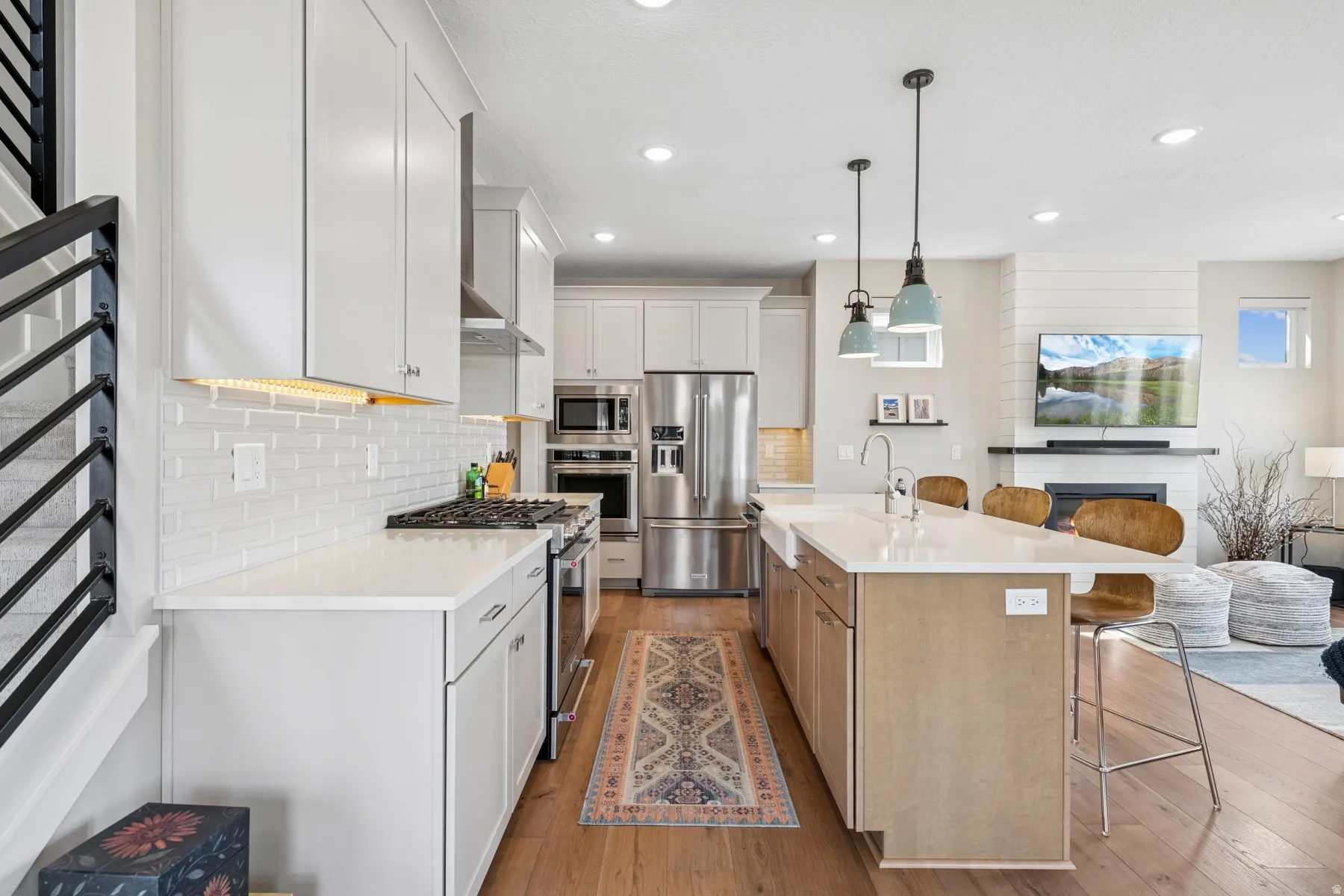 Open-concept kitchen featuring wood-finish flooring, white cabinetry, a large kitchen island with seating, a built-in oven, and a stainless steel refrigerator