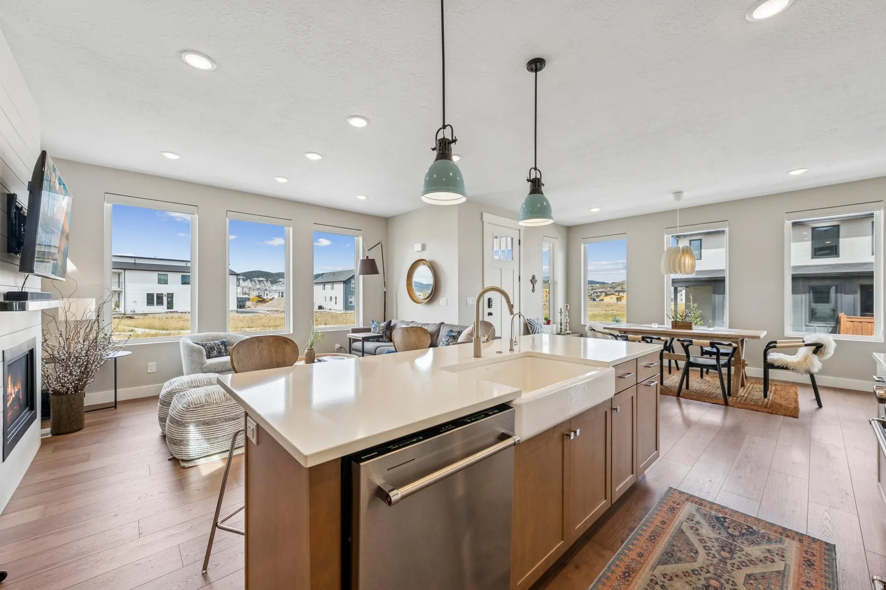 Open-concept living space featuring wood-finish flooring, recessed lighting, a built-in fireplace, and an island with an integrated farmhouse sink and stainless steel dishwasher