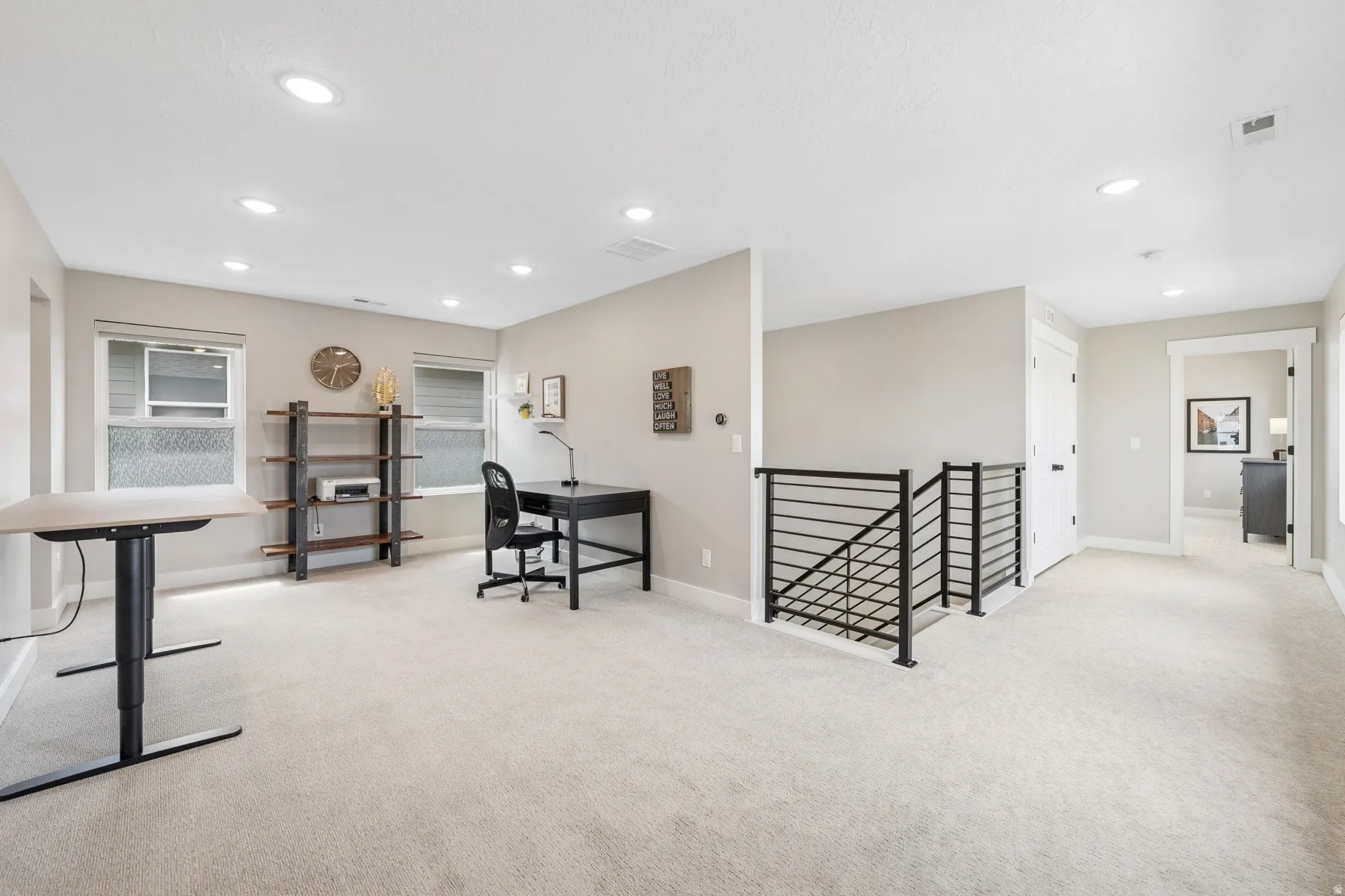 Expansive carpeted area with recessed lighting, multiple windows, and a contemporary black metal stair railing
