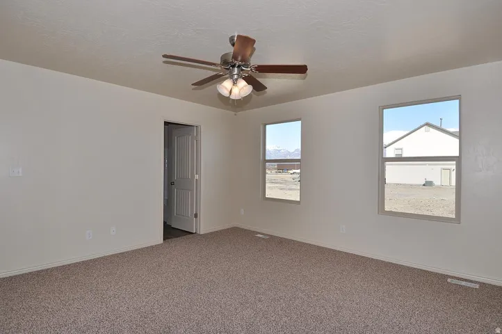 Neutral-toned wall paint, two windows, carpeted flooring, and a ceiling fan with integrated lighting
