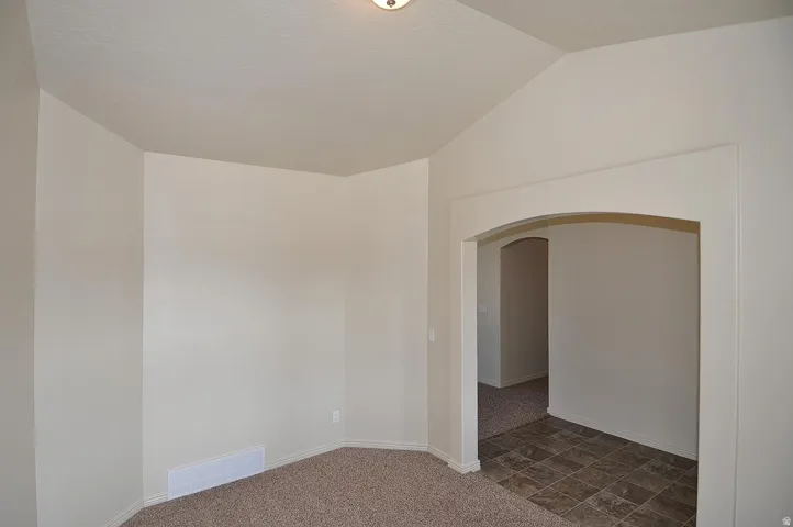 Carpeted flooring, vaulted ceiling, arched doorway with trim, light-toned walls, and tiled flooring