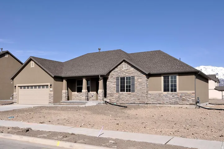Stucco exterior with stone accents, covered front entry, attached garage with a panel door, and multiple windows with dark shutters