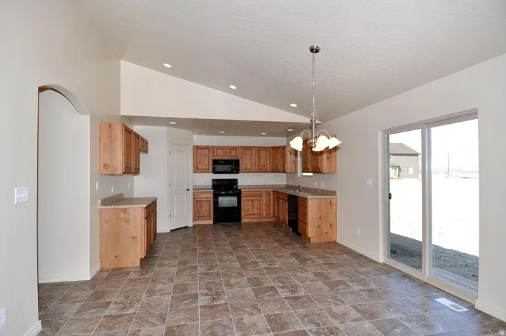 Kitchen and dining area featuring vaulted ceilings, recessed lighting, wood cabinetry, dark appliance package, and sliding glass door