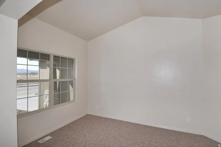 Vaulted ceiling, grid-pattern window, neutral wall paint, textured carpet flooring, base molding