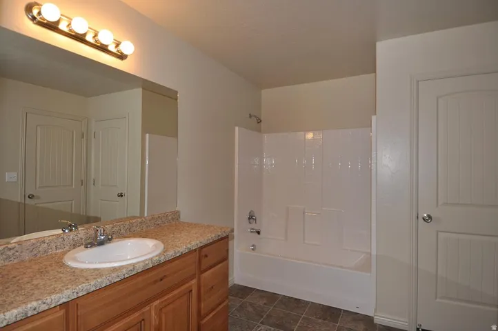 Bathroom featuring a wood-finish vanity with a speckled countertop, a large wall mirror, and a built-in bathtub with a white tiled surround