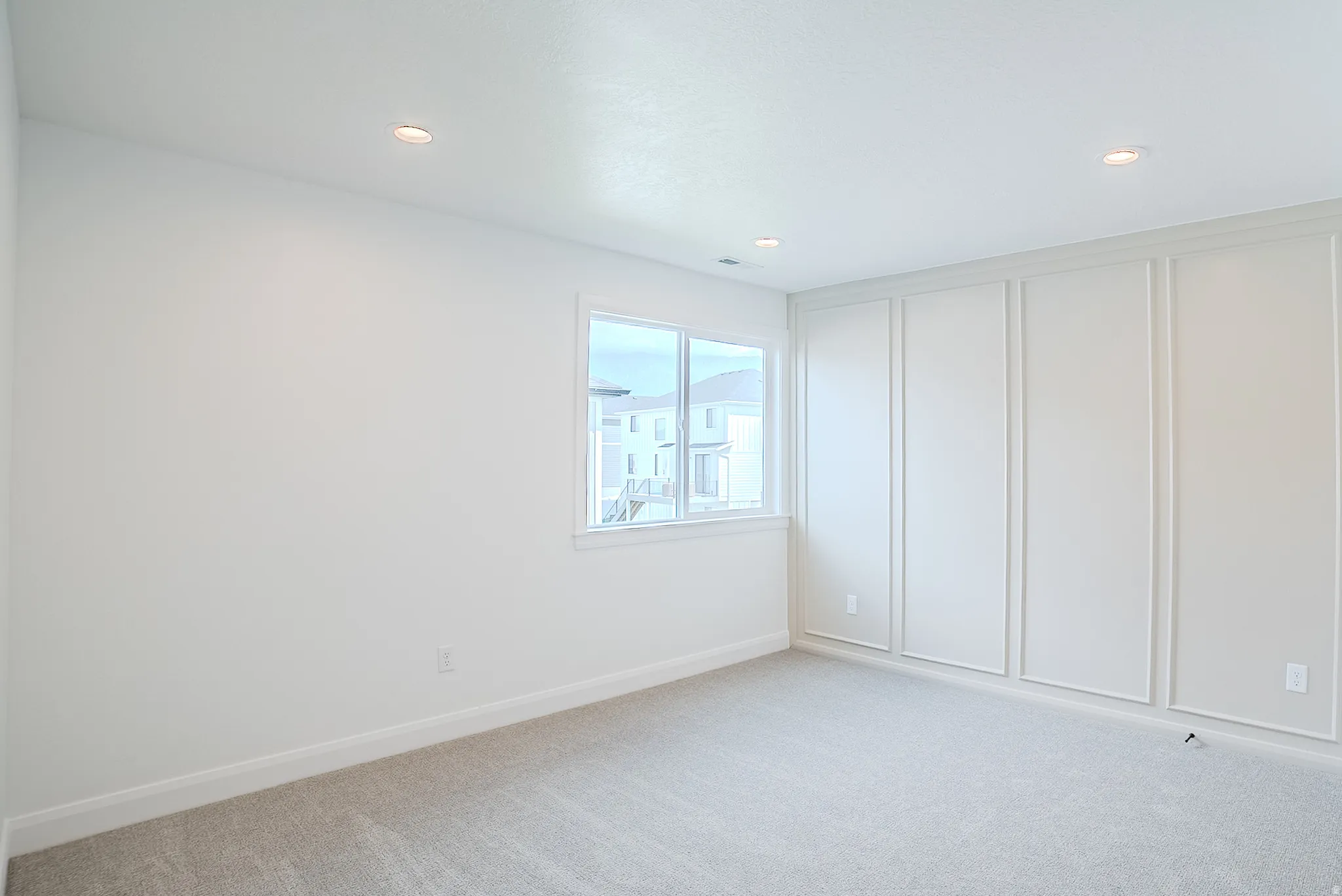 Recessed lighting, light-toned carpeting, and a window with white trim