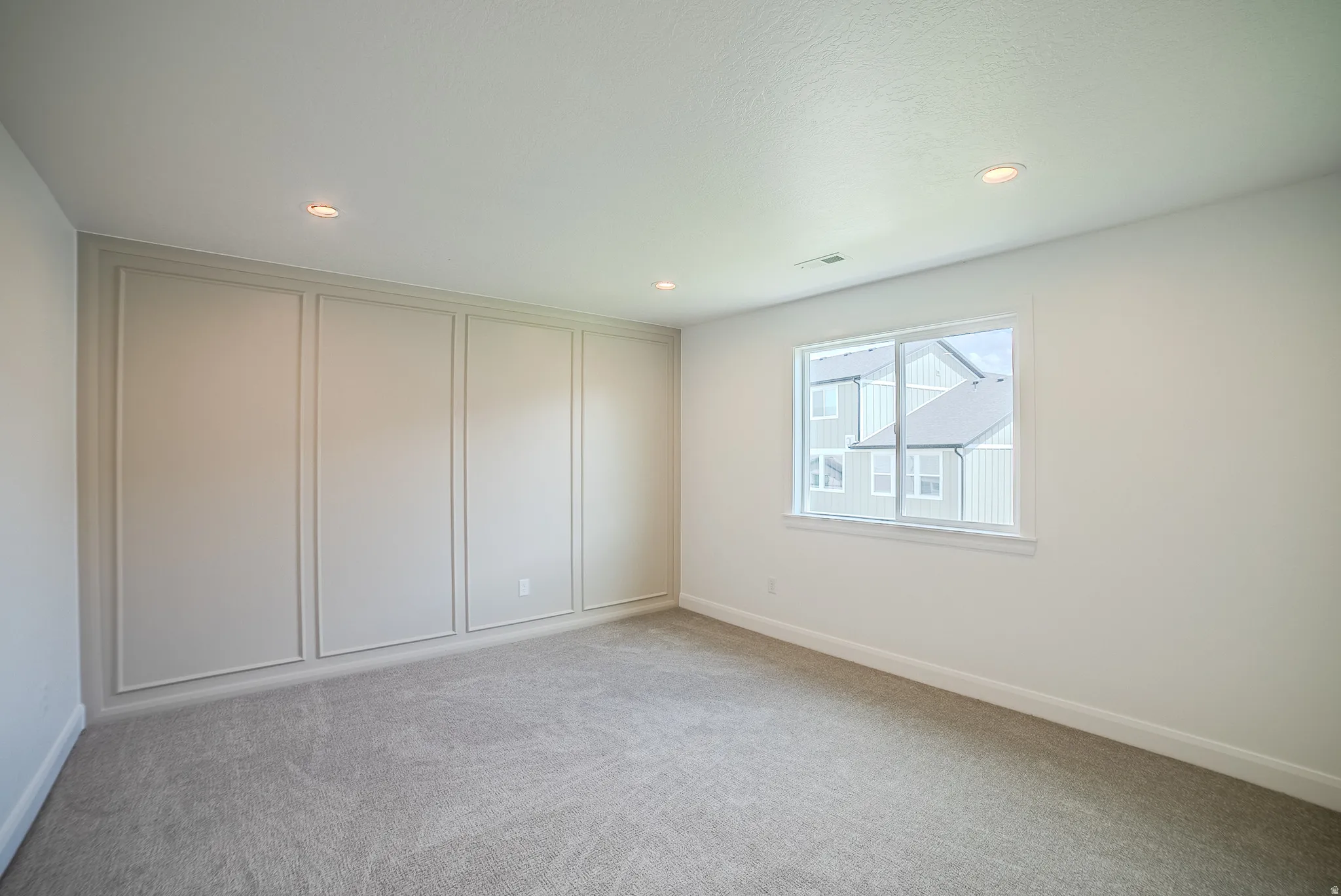 Recessed lighting, light gray carpeting, and an accent wall with decorative molding