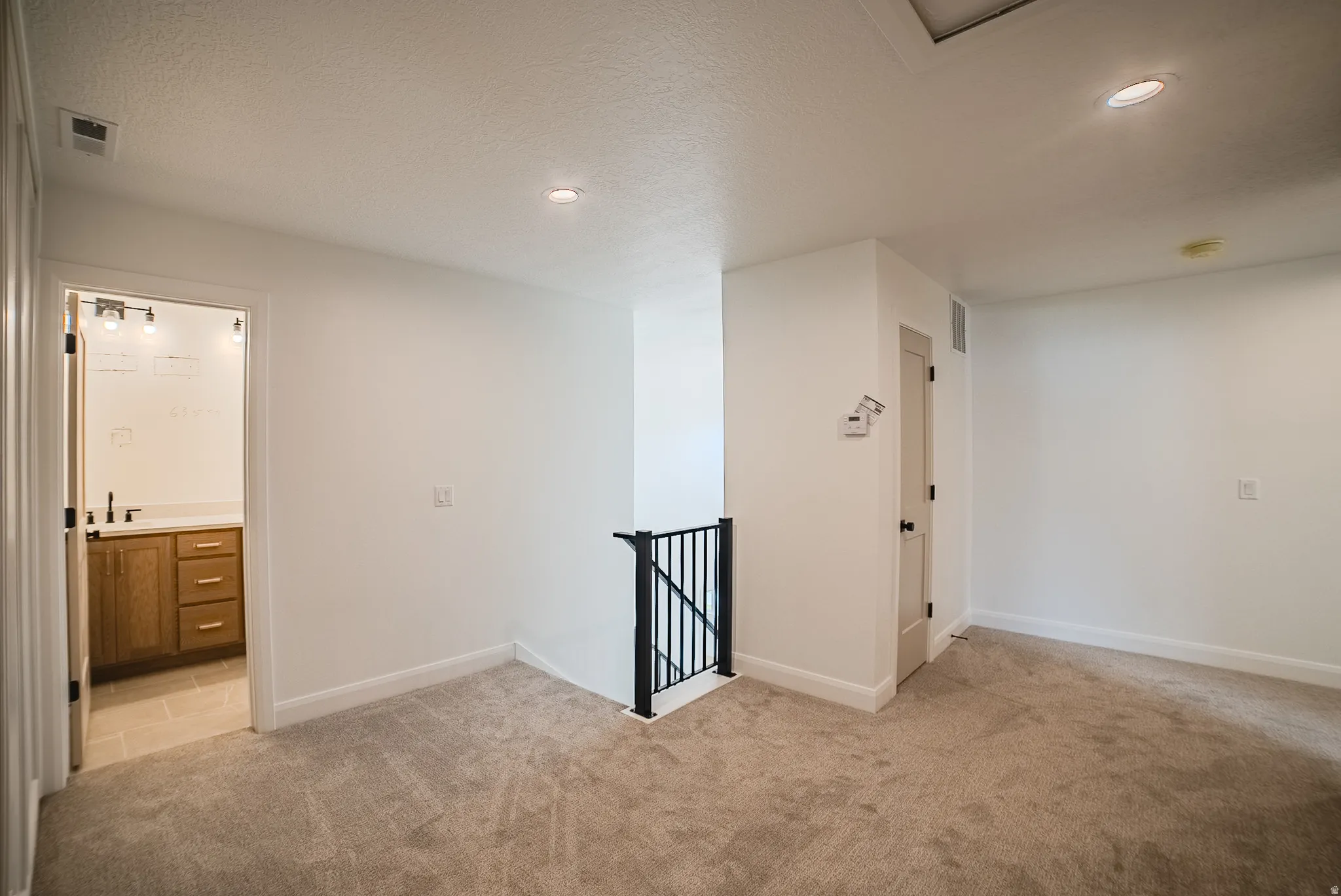 Recessed ceiling lighting, light-colored carpeting, a black metal staircase railing, a light wood-finish vanity with a light countertop, and a tiled bathroom floor
