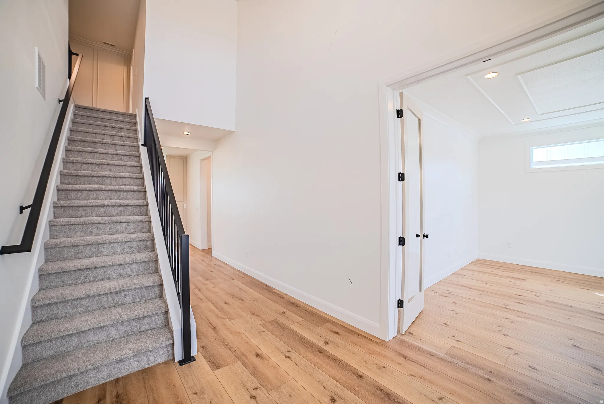 Carpeted staircase with black metal railings, wood-finish flooring, white walls, and a recessed ceiling with accent lighting