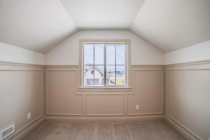 Window with muntins, wainscoting, vaulted ceiling, and carpet flooring