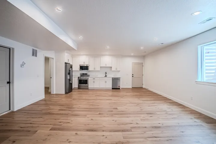 Open-concept room featuring wood-finish flooring, recessed lighting, and a kitchen with white cabinetry